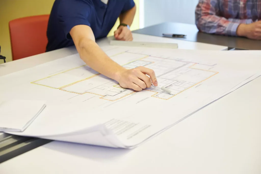 Man pointing to a point on the plan of a technical drawing of a building